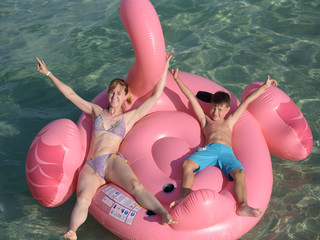 European woman and her son swimming in sea at resort on huge inflatable pink flamingo. They on summer vacations.