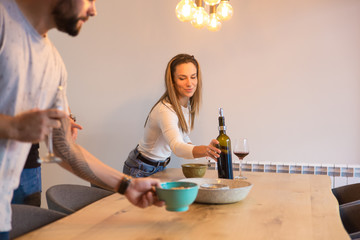 Smiling friends putting snacks and red wine on table. Cheerful young people spending time together. Leisure, friendship concept