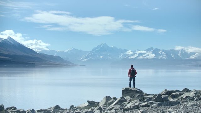 Mountain view, Lake Pukaki, New Zealand. Young adventure photographer climbs rock, taking photos of the  spectacular view with Mt Cook in distance.