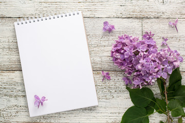 Clean notepad with spring lilac flowers on white wooden background