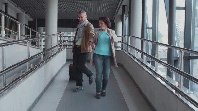 Happy elderly senior couple of travelers with suitcase walking in airport walkway