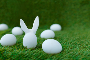 Fototapeta na wymiar White chicken eggs on green grass, behind which are hidden the ears of the Easter bunny, which are symbols for the celebration of religious holiday among Christians and Catholics.