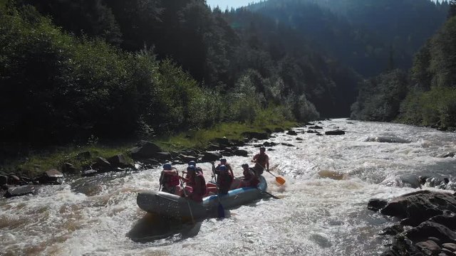 People in inflatable boat rafting by rapid river. Kayakers floating on fast flowing river in mountains. Carpathians, Ukraine.