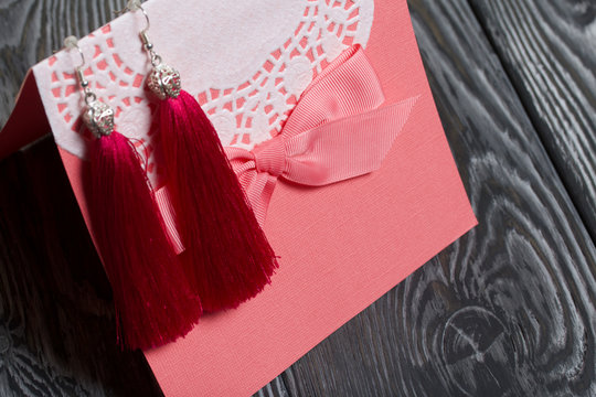 Homemade red tassel earrings and a greeting card. They lie on brushed pine boards painted in black and white.