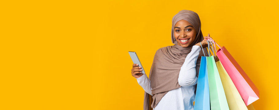 Happy Afro Muslim Girl In Headscarf Holding Smartphone And Shopping Bags