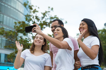 Group of cheerful young people posing for selfie. Smiling friends waving to camera phone. Concept of self portrait