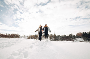 Cute girls walking in a winter park. Sisters have fun with snow. Ladies in a cute hats