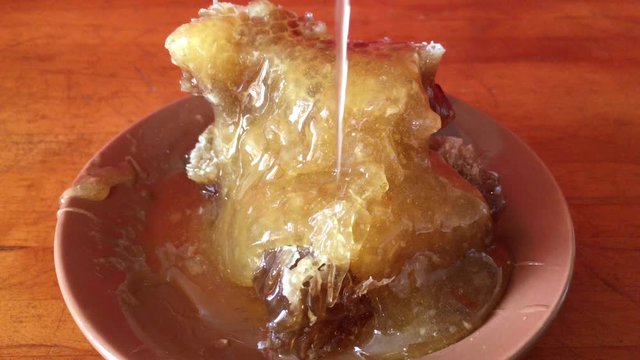 natural golden honey is poured on honeycombs in a clay brown plate on a wooden table