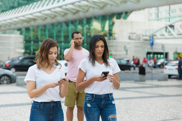 Two women walking on street with phones. Smiling friends holding smartphones while strolling. Communication and technology concept