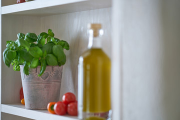 closeup kitchen shelf olive oil bottle pot parsley in mediterranean style, green yellow red vegetarian vegetable in sunny summer feeling,copy space blurred