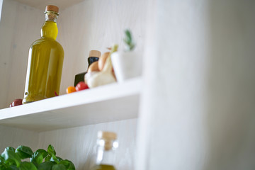 closeup kitchen shelf olive oil bottle pot parsley in mediterranean style, green yellow red vegetarian vegetable in sunny summer feeling,copy space blurred