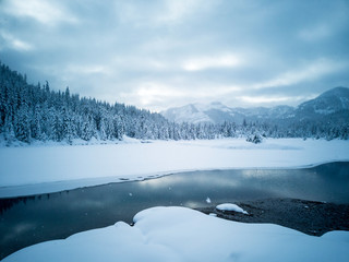 Snow covered frozen beautiful Gold Creek Pond with snow covered trees and trail during the winter in the Alpine Lakes Wilderness in Kittitas county Washington State