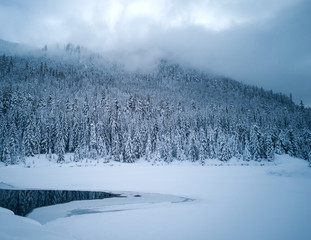 Snow covered frozen beautiful Gold Creek Pond with snow covered trees and trail during the winter in the Alpine Lakes Wilderness in Kittitas county Washington State
