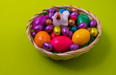Fototapeta na wymiar Osternest gefüllt mit bunten Eiern und weissem Hahn auf grünem Hintergrund