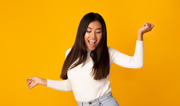 Playful asian girl dancing on yellow studio background