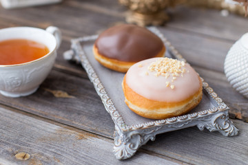 Donuts made of white milk chocolate, coated with glaze and nuts. Aristocratic tea party with porcelain cup on wooden table. Decorated with vases,cotton inflorescences,white sugar bowl.Gold background