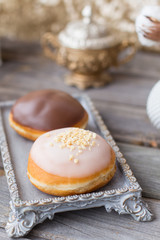 Donuts made of white milk chocolate, coated with glaze and nuts. Aristocratic tea party with porcelain cup on wooden table. Decorated with vases,cotton inflorescences,white sugar bowl.Gold background