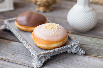 Donuts made of white milk chocolate, coated with glaze and nuts. Aristocratic tea party with porcelain cup on wooden table. Decorated with vases,cotton inflorescences,white sugar bowl.Gold background
