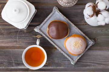 Donuts made of white milk chocolate, coated with glaze and nuts. Aristocratic tea party with porcelain cup on a wooden table background. Decorated with vases, cotton inflorescences, white sugar bowl