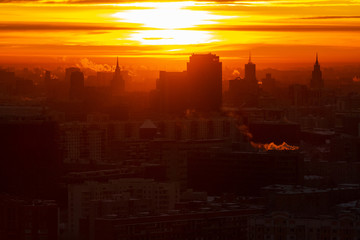 Fototapeta premium Sunrise over the city. Aerial view of Moscow, silhouettes of buildings in downtown with colorful lighting sunrise sky and soft clouds. Factories pipe, of which there are smoke. Rising sun