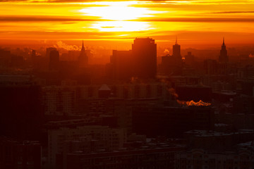 Sunrise over the city. Aerial view of Moscow, silhouettes of buildings in downtown with colorful lighting sunrise sky and soft clouds. Factories pipe, of which there are smoke. Rising sun
