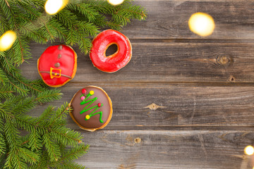 Christmas flat lay with donuts with icing and red, white, pink milk chocolate topping, in the design of Santa Claus, new year tree. Wooden table background. Spruce green branches and garland lights