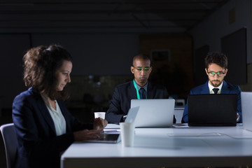 Focused business team working at night in office. Concentrated office managers working with laptops. Overwork, working late concept