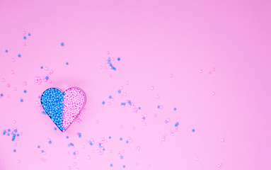 On a pink background, a metal heart shape is filled with decorative beads.