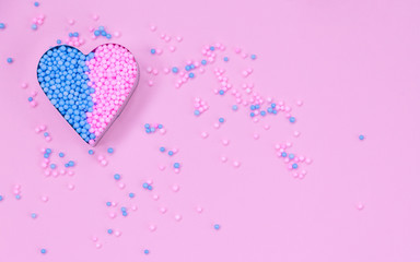 On a pink background, a metal heart shape is filled with decorative beads.