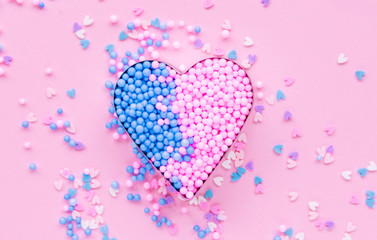 On a pink background, a metal heart shape is filled with decorative beads.