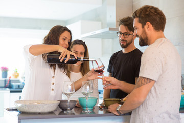 Beautiful young woman pouring wine in glasses. Group of cheerful people standing near table. Wine tasting concept