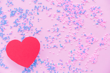 Paper red heart on a background of decorative balls in blue and pink
