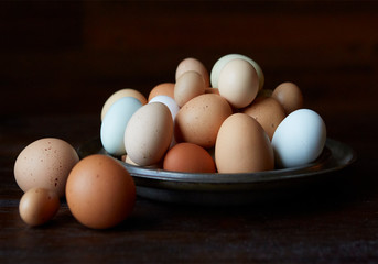 Large metal bowl with various size and colored eggs in it and on the tabletop