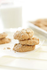 Stack of three sunflower seed cookies sitting on white parchment paper with a glass of milk and pan of cookies in the background