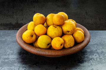 Ceramic bowl full of small and round Japanese quinces placed on the table. Dark (black and gray) background.