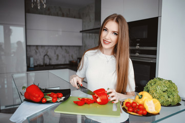 Woman in a kitchen. Blonde in a white t-shirt. Woman with vegetables
