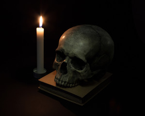 Human skull and candle on old book isolated on black