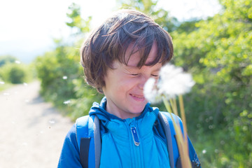 The boy is blowing on a dandelion.