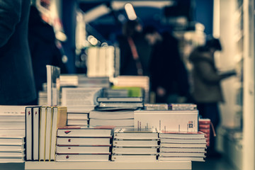 Pile of books, abstract blurred background in book store or in library. Unrecognizable people,...
