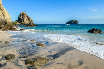 A black and white sand beach, gently washed by waves on an idyllic Koka Beach. Hidden gem of Flores, Indonesia. There are some boulders in the sea. Escaping from it all. Beauty in the nature