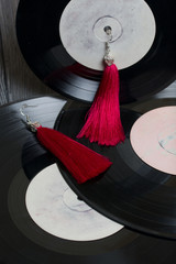 Homemade tassel earrings in red. Against the background of old vinyl records and brushed pine...