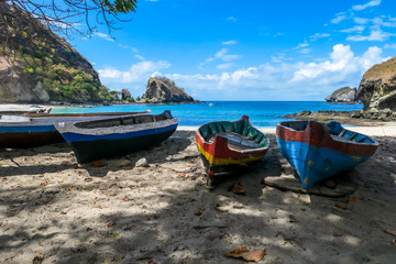 Fototapeta na wymiar A row of colorful boats parked on a shore of idyllic Koka Beach in Flores, Indonesia. The boats are lined up under the trees, in the shade. There are some cliffs in the back. Hidden gem of Indonesia.