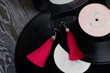 Homemade tassel earrings in red. Against the background of old vinyl records and brushed pine...