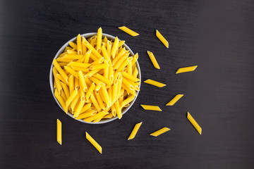 Top view of black background with italian raw penne or pasta in bowl with copy space