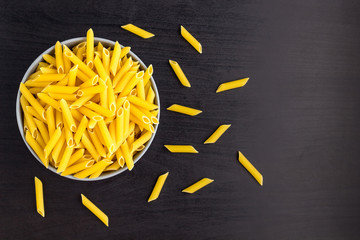 Top view of black background with italian raw penne or pasta in bowl with copy space