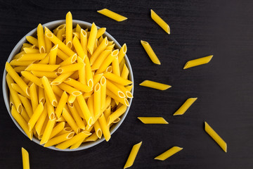 Top view of black background with italian raw penne or pasta in bowl with copy space