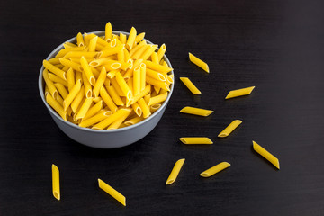 black background with italian raw penne or pasta in bowl with copy space