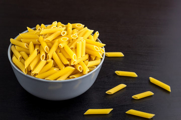 black background with italian raw penne or pasta in bowl with copy space