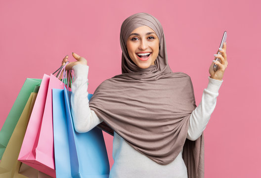 Joyful Arabic Woman In Hijab Holding Smarphone And Bright Shopping Bags