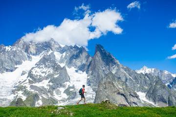 A trail runner running below the high snowy mountains along a grassy ridge in the Alps along the Tour du Mont Blanc route. - 316854137